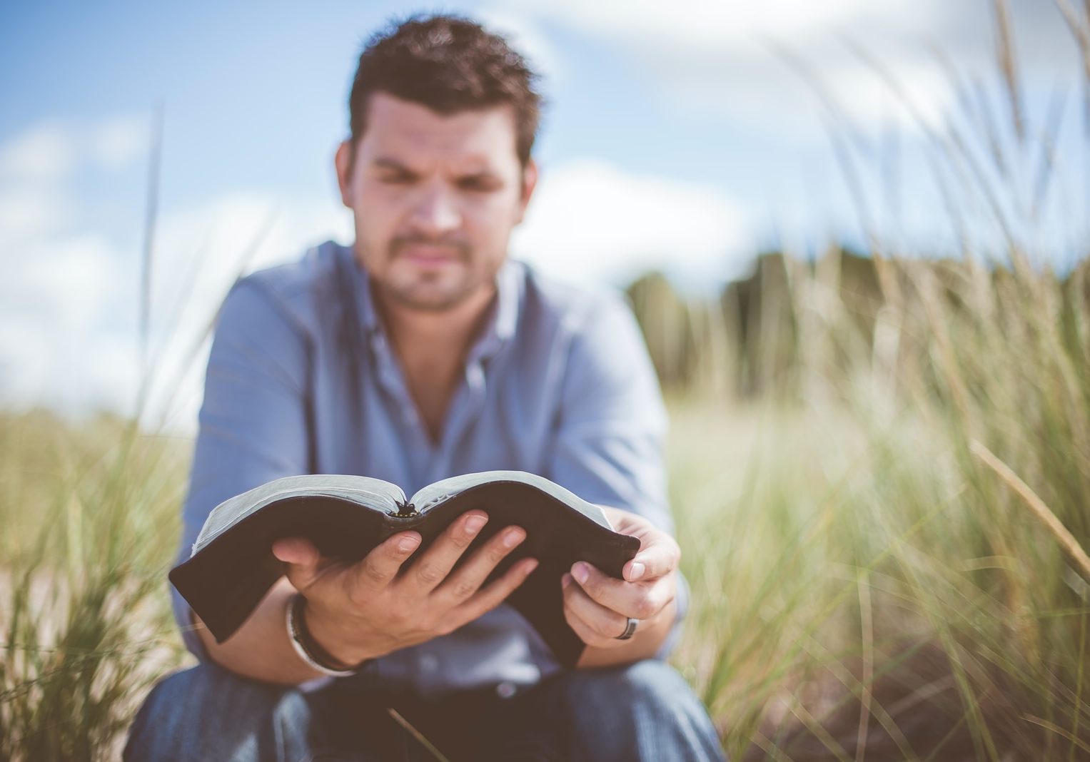 man reading book in grass field